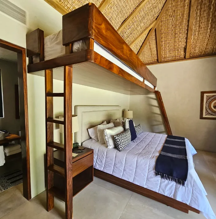 Custom wooden bunk bed with a ladder and woven upper panels in a Punta Mita carpentry project.